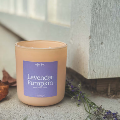 Candle with a lavender pumpkin label on a concrete surface with dried lavender and leaves.