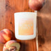 Candle labeled 'Big Peach Energy' surrounded by peaches on a wooden surface