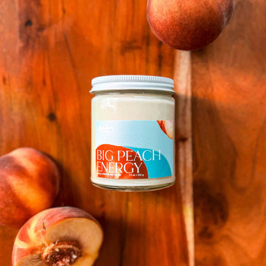 Candle named 'Big Peach Energy' on a wooden surface with peaches around