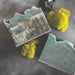 Obsidian Mist soap bar with packaging on a dark surface with greenery.