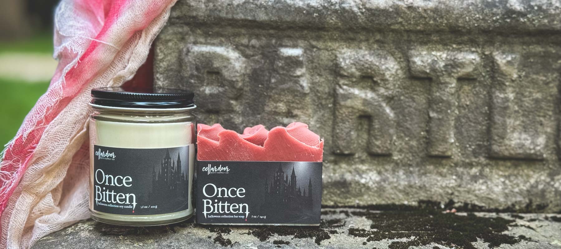 Candle labeled 'Once Bitten' with packaging on a stone surface.