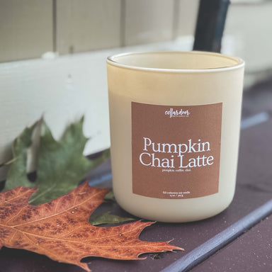 Candle labeled 'Pumpkin Chai Latte' on a surface with leaves
