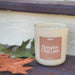 Candle labeled 'Pumpkin Chai Latte' on a surface with leaves in the background