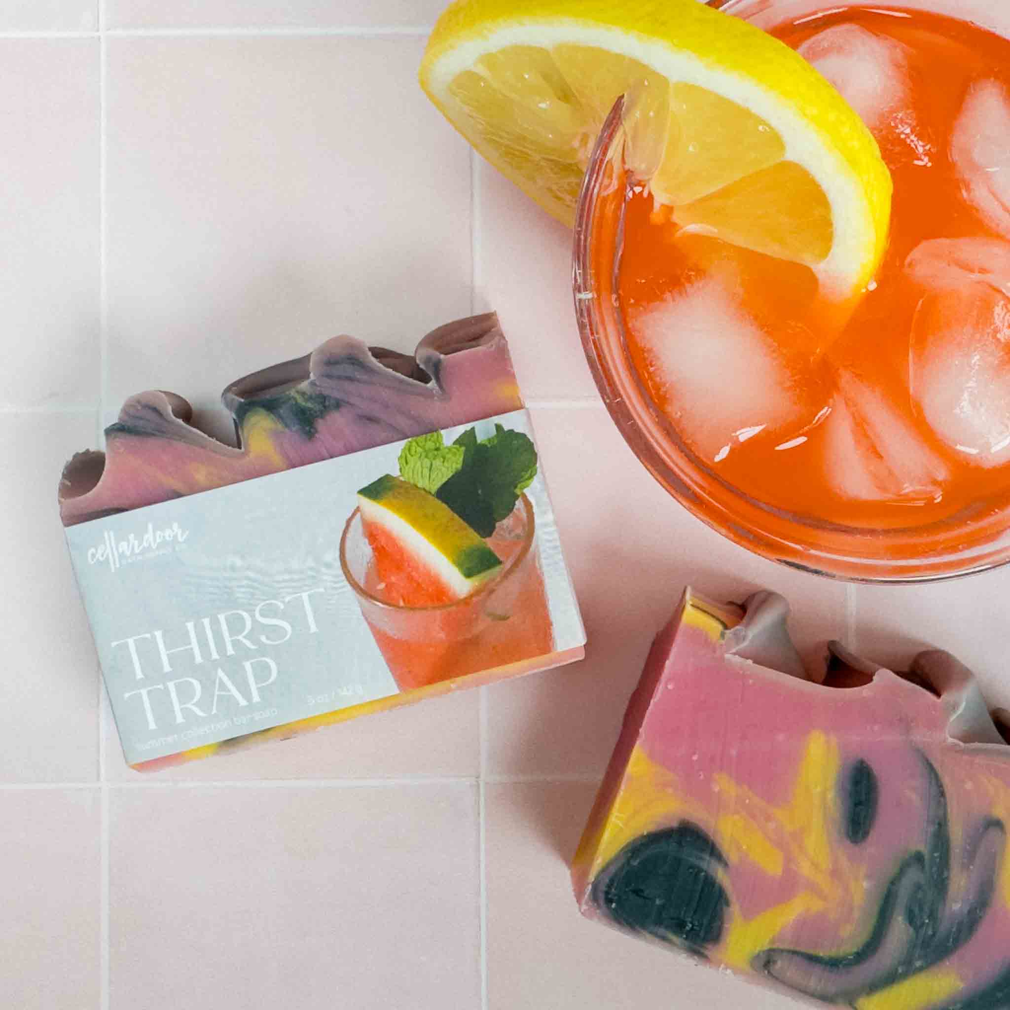 Colorful soap bars named Thirst Trap with a drink and lemon slice on a tiled surface