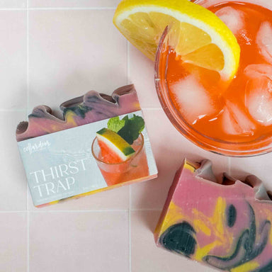 Colorful soap bars named Thirst Trap with a drink and lemon slice on a tiled surface