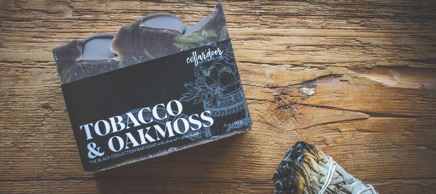 A brown and yellow soap named Tobacco & Oakmoss rests on a rustic wood background.